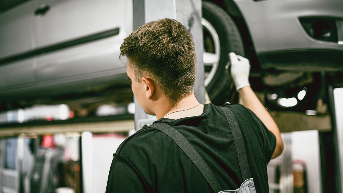 A male trainee is infront of a car which is on a llifting platform (Source: iStock | AleksandarGeorgiev) A male trainee is infront of a car which is on a llifting platform