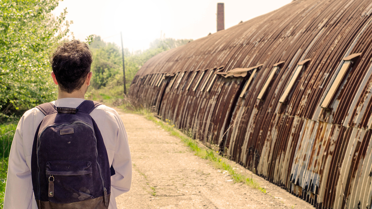 A man with a backpack walks next to a  barrack (Source: iStock | RobertoDavid) A man with a backpack walks next to a  barrack