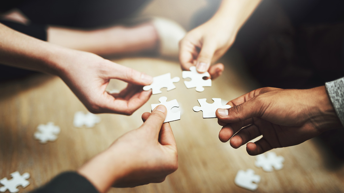 Close up of four hands, each holding a piece of the puzzle and folding it together (Source: iStock | PeopleImages) Close up of four hands, each holding a piece of the puzzle and folding it together